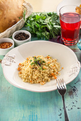 Cous cous with carrot in white bowl with glass of red drink on blue wooden table