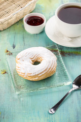 Cream puff rings with powdered sugar choux pastry and cup of black tea on blue wooden table