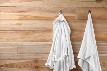 Soft comfortable bathrobe and towel hanging on wooden wall. Space for text