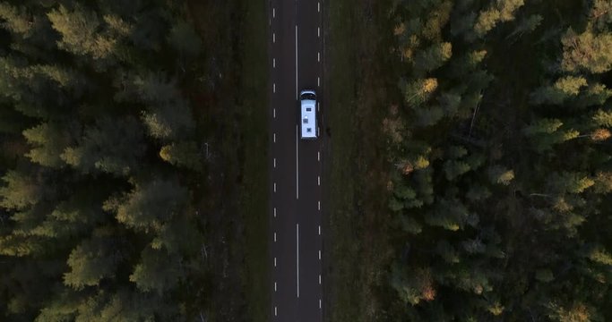 Camper van on a forest road, aerial, top down, drone shot, above a rv car, driving on road 99, at sunset, in middle of foliage trees, on a sunny autumn evening, in Norrland, Swedish Lappland, Sweden