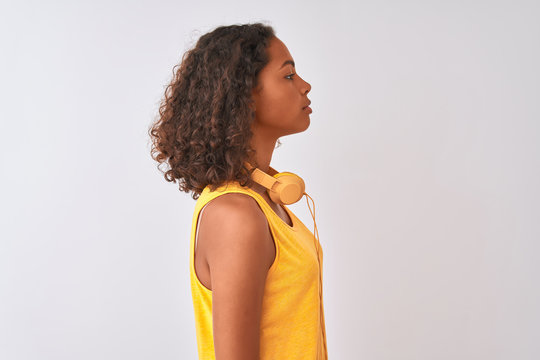 Young brazilian woman wearing yellow headphones over isolated white background looking to side, relax profile pose with natural face with confident smile.
