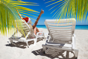 Happy woman in Santa Helper Hat lie on sunbed showing  thumbs up at the beach