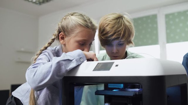 Education in the modern school, children learn modeling, boy and girl watching of process 3D printer prints.