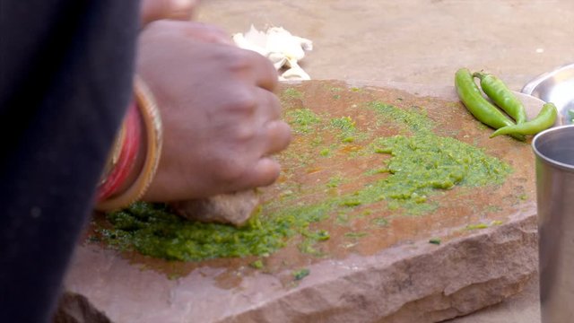 An Indian woman making the chili paste on sil batta (stone grinder). HD video of a rural Indian woman grinding chilies on a stone and making green chutney for the meal