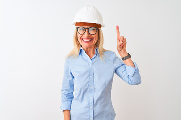 Middle age architect woman wearing glasses and helmet over isolated white background showing and pointing up with finger number one while smiling confident and happy.