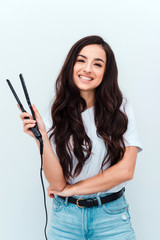 Fototapeta premium Portrait of pretty cute girl using a straightener for her curly hair, isolated on white background