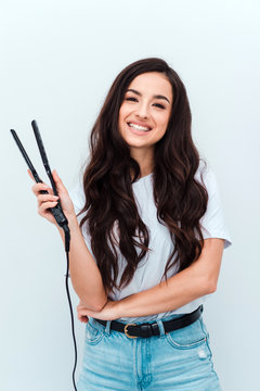 Portrait of pretty cute girl using a straightener for her curly hair, isolated on white background