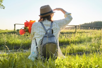 Woman in hat with backpack flowers sitting back on the grass enjoying summer nature