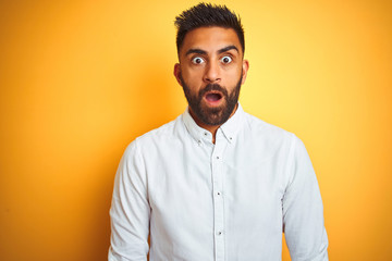 Indian businessman wearing white elegant shirt standing over isolated yellow background afraid and shocked with surprise expression, fear and excited face.