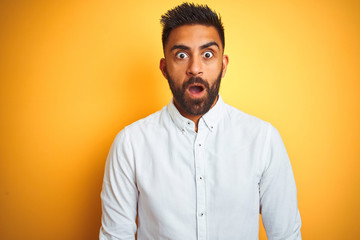Obraz premium Indian businessman wearing white elegant shirt standing over isolated yellow background afraid and shocked with surprise expression, fear and excited face.