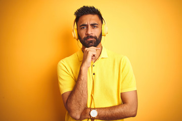 Arab indian hispanic man listening to music using headphones over isolated yellow background serious face thinking about question, very confused idea