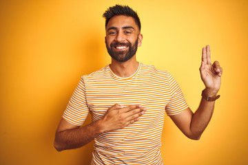 Young indian man wearing t-shirt standing over isolated yellow background smiling swearing with...