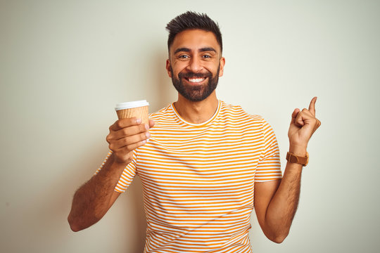 Young indian man drinking cup of coffee standing over isolated white background very happy pointing with hand and finger to the side