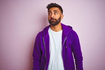 Obraz premium Young indian man wearing purple sweatshirt standing over isolated pink background smiling looking to the side and staring away thinking.