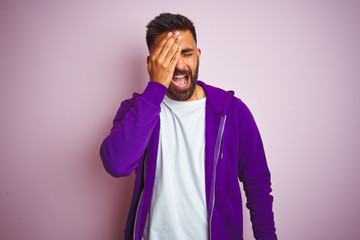Fototapeta premium Young indian man wearing purple sweatshirt standing over isolated pink background Yawning tired covering half face, eye and mouth with hand. Face hurts in pain.