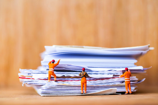 miniature worker climbing on stack of messy work sheet and  document on wooden table.