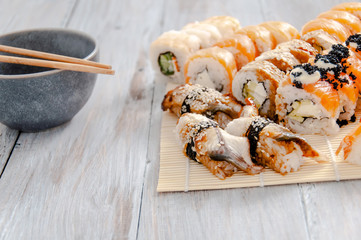 Sushi and soy sauce in a bowl and wooden chopsticks on a gray wooden table. Japanese food. Sushi Set. Variety of rolls. Menu.