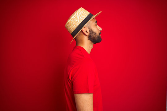 Young handsome indian man wearing t-shirt and hat over isolated red background looking to side, relax profile pose with natural face with confident smile.