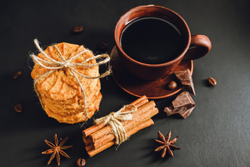 Homemade cookies, cup with hot coffee, chocolate pieces, cinnamon sticks, star anise on dark...