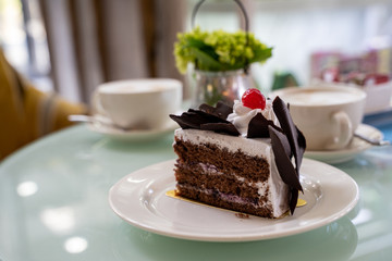 Delicious three layer chocolate cake with shavings and a cherry on a plate at a cafe