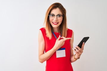 Naklejka premium Redhead businesswoman wearing id card using smartphone over isolated white background very happy pointing with hand and finger