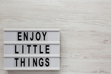 'Enjoy little things' words on a lightbox on a white wooden surface, top view. Overhead, from above, flat lay. Copy space.