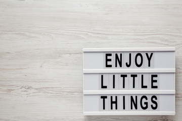 'Enjoy little things' words on a modern board on a white wooden background, top view. Overhead, from above, flat lay. Space for text.