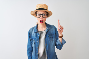 Redhead woman wearing denim shirt glasses and hat over isolated white background pointing finger up with successful idea. Exited and happy. Number one.