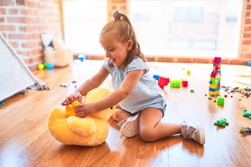 Young beautiful blonde girl kid enjoying play school with toys at kindergarten, smiling happy playing with stuffed animal at home