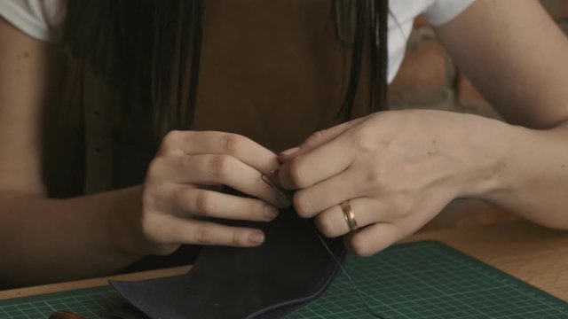 Professional female skinner working with genuine leather at workshop. Leather master sewing with needle and strings. Handmade and leatherwork concept.