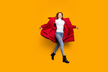 Full length photo of charming lady jumping high walking street amazing sunny fall day wear jeans shoes white pullover red long winter coat isolated yellow color background © deagreez