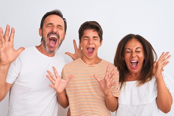 Family of three, mother, father and son standing over white isolated background celebrating mad and...