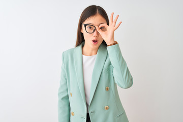 Chinese businesswoman wearing elegant jacket and glasses over isolated white background doing ok gesture shocked with surprised face, eye looking through fingers. Unbelieving expression.