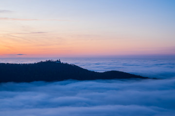 Fototapeta na wymiar Germany, Magical aerial view above fog clouds in valley of swabian alb nature landscape at sunset with orange sky near stuttgart with view to castle teck
