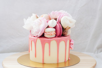 White cake with pink melted chocolate, fresh roses and peonies, macaroons and meringues. 