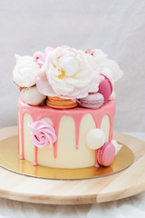 White cake with pink melted chocolate, fresh roses and peonies, macaroons and meringues. 