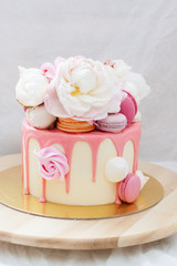 White cake with pink melted chocolate, fresh roses and peonies, macaroons and meringues. 