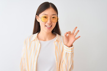 Young chinese woman wearing striped shirt and glasses over isolated white background doing ok sign with fingers, excellent symbol