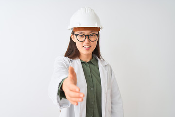 Young chinese engineer woman wearing coat helmet glasses over isolated white background smiling friendly offering handshake as greeting and welcoming. Successful business.