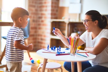 Beautiful teacher and toddler boy playing with figurine army soldiers at kindergarten