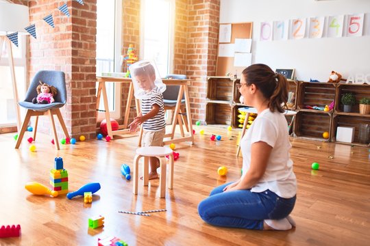 Beautiful teacher and toddler boy playing with plastic basket at kindergarten