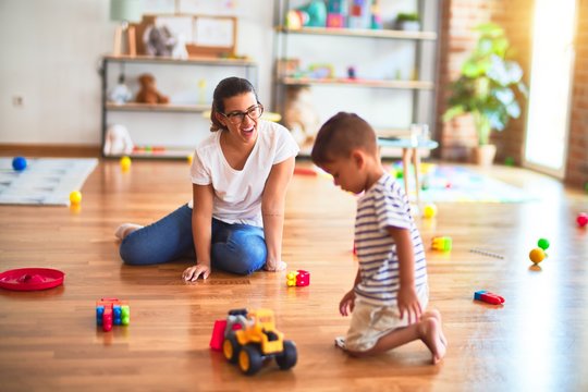 Beautiful teacher and toddler boy playing with tractor and cars at kindergarten