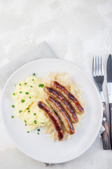 Roasted nuremberg sausages served with sour cabbage and mashed potatoes, on white plate, vertical, top view, copy space