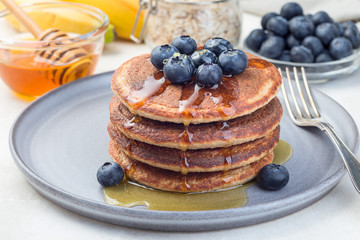 Healthy oatmeal banana pancakes garnished with blueberry and honey, on gray plate, horizontal
