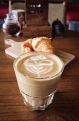 A cup of coffee with latte art on top and butter  croissant