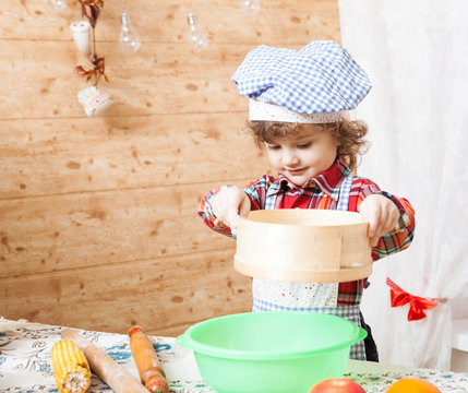 Portrait of a crispy boy in chef clothes in the kitchen interior. Child culinary busy preparing food.
