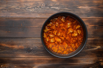 Homemade traditional Hungarian goulash dish in a saucepan against a wooden background