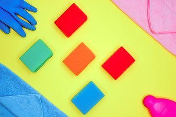 Cleaning tools layout. on a yellow background lies a layout of different color sponges, microfiber cloths, rubber glove and detergent for cleaning the kitchen cleaning dishes flatlay