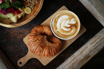 A cup of coffee with latte art on top, butter  croissant and granola with fresh tropical fruits and yogurt on table in caffee, top view. Concept of healthy breakfast