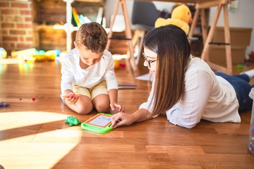 Fototapeta premium Beautiful teacher and toddler drawing using digital board around lots of toys at kindergarten